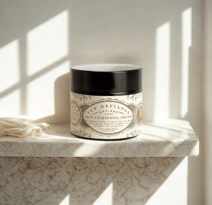 Napiers Age Defiance Skin Lightening Cream displayed on a sunlit marble surface, a vegan herbal moisturiser formulated with chamomile, chickweed, lemon and licorice root to brighten skin tone, soothe sensitivity and support mature, radiant skin.