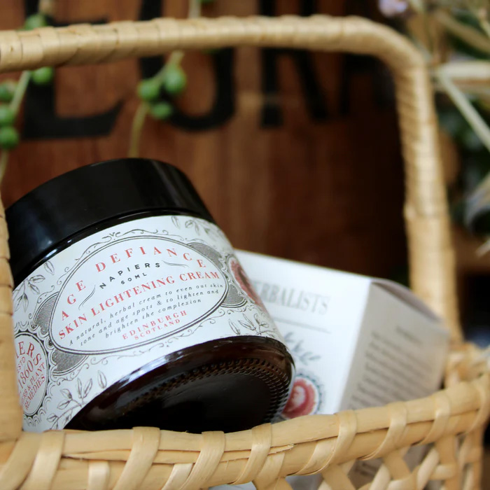 Napiers Age Defiance Skin Lightening Cream nestled in a woven basket, showcasing a vegan herbal moisturiser formulated with chamomile, chickweed, lemon and licorice root to brighten skin tone, soothe sensitivity and revitalise mature skin naturally.