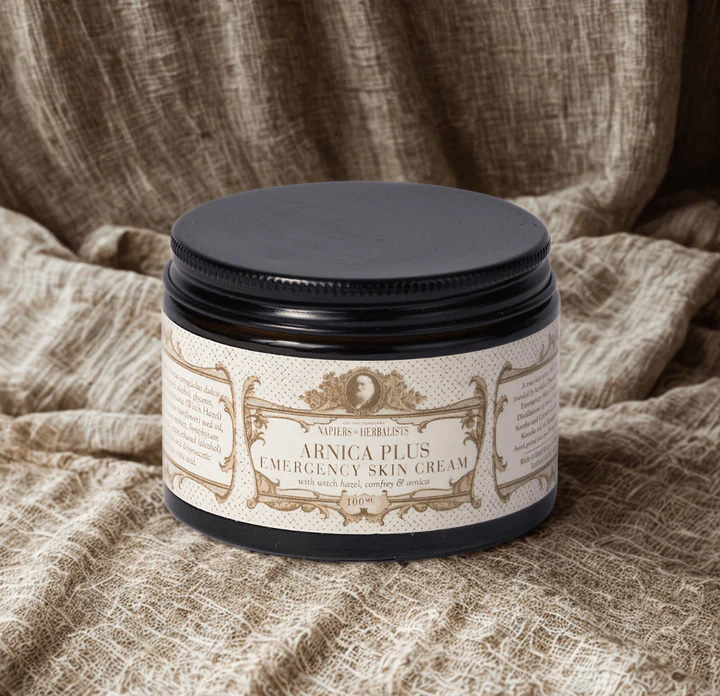 Napiers Arnica Plus Emergency Skin Cream in a black jar, displayed on natural fabric, featuring a herbal formula with arnica, witch hazel and comfrey to support skin comfort and provide soothing relief for muscles and joints.