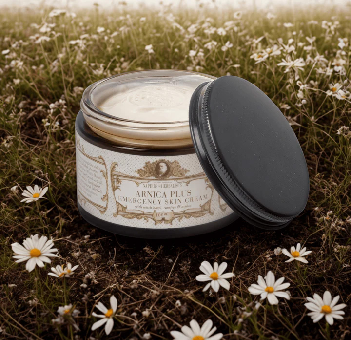 Open jar of Napiers Arnica Plus Emergency Skin Cream placed in a meadow with daisies, showcasing a natural herbal cream made with arnica, witch hazel and comfrey to soothe skin and provide gentle relief for muscles and joints.