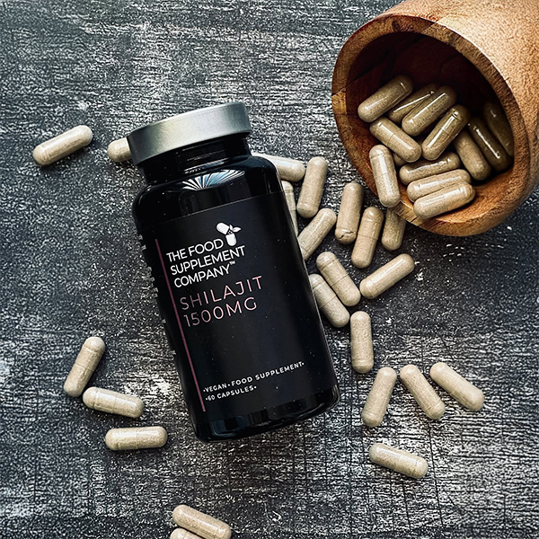 The Food Supplement Company Shilajit 1500mg capsules bottle displayed on a textured surface with loose capsules spilling from a wooden bowl, highlighting high-strength Himalayan shilajit supplement in vegan capsules for energy, stamina, and cognitive support.
