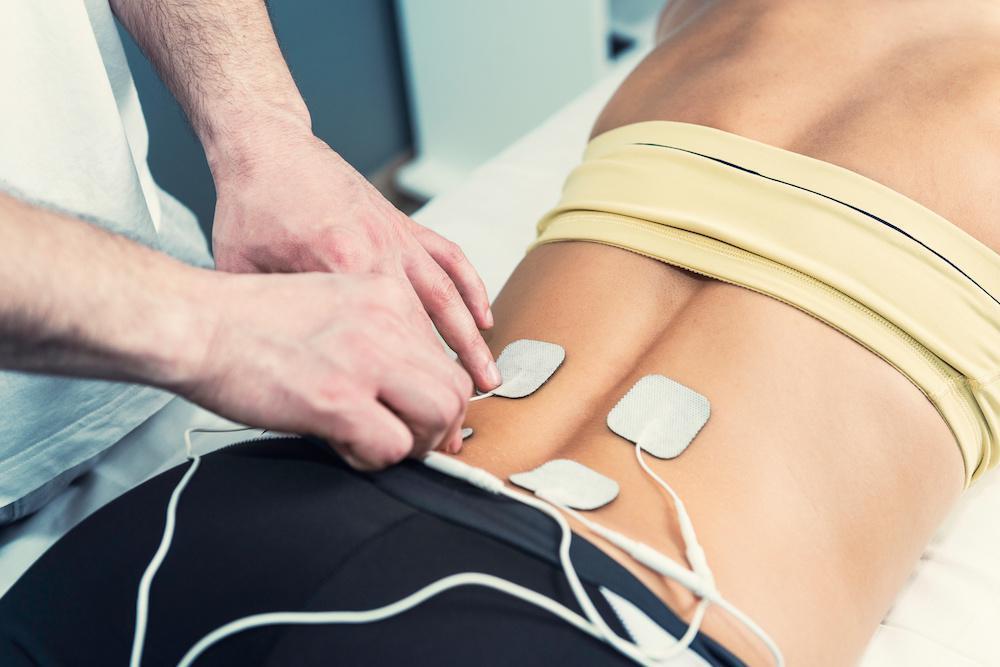 A Guide to Drug-Free Pain Relief-StressNoMore. Therapist placing TENS electrode pads on a person’s lower back, illustrating electrical stimulation therapy for pain relief, muscle relaxation and physiotherapy treatment.