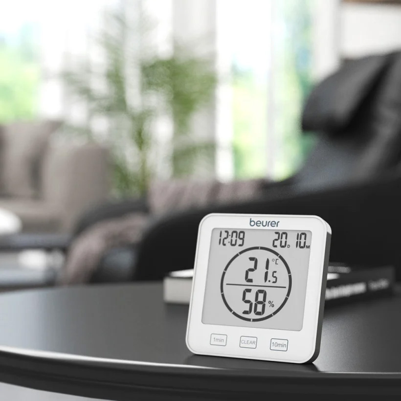 Beurer HM 22 digital thermo hygrometer displayed on a living room table, showing indoor temperature and humidity levels on a clear LCD screen, ideal for monitoring air quality, comfort, and humidity in the home or office.