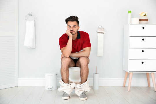 4 Mistakes You're Making When You Go to the Toilet-StressNoMore. Man sitting on a toilet in a modern bathroom looking frustrated, representing constipation, straining or difficulty with bowel movements.