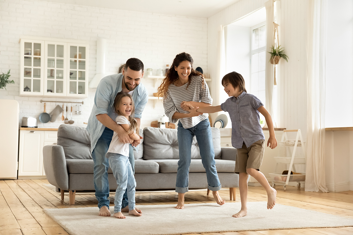 Do You Need to Improve the Air Quality in Your Home?-StressNoMore. Smiling family playing together in a cosy, bright living room, symbolising happiness, wellbeing, active home life and positive family bonding.