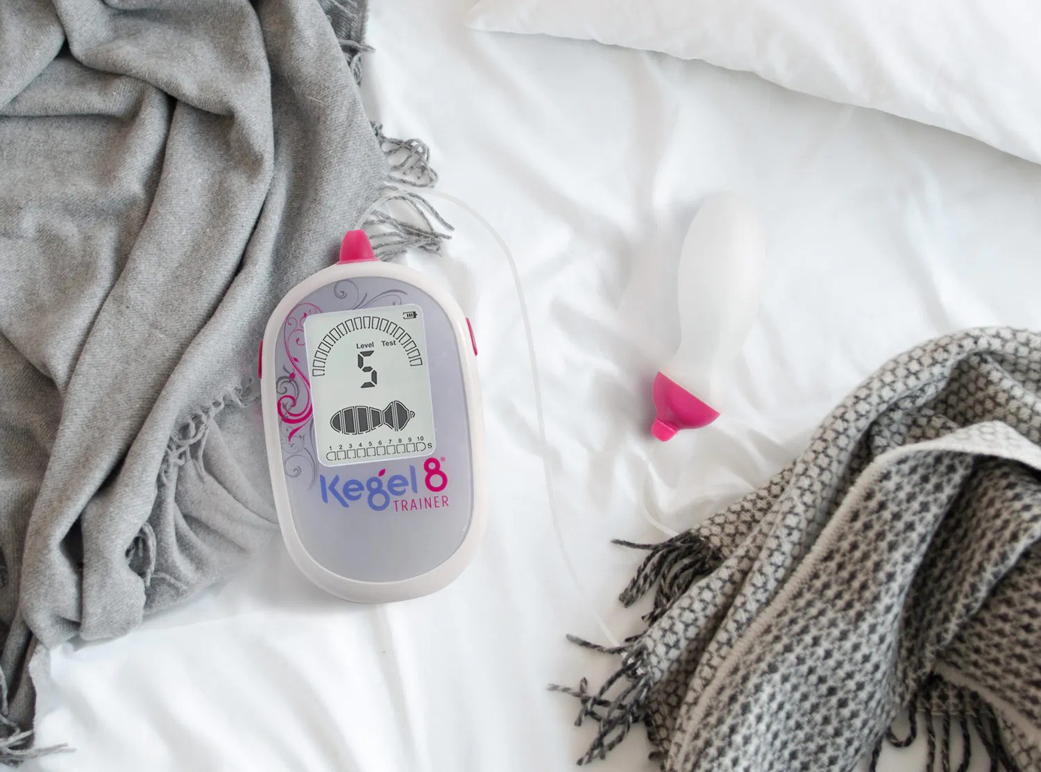 Kegel8 pelvic floor exerciser device displayed on a bed with fabric and accessories, showing the squeeze scale reading on the screen, used to illustrate pelvic floor strength assessment. What's Your Squeeze Scale?-StressNoMore