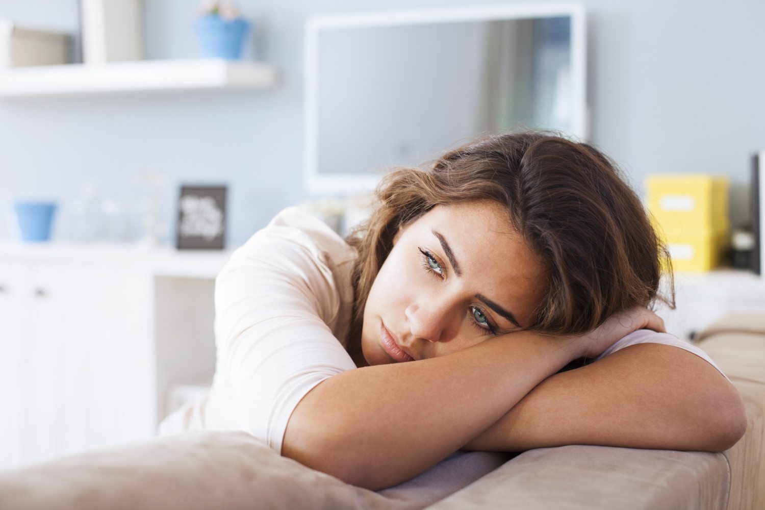 Sick and Tired of Feeling Tired? Tips for Better Sleep-StressNoMore. Woman resting her head on her arms while looking distressed or fatigued, representing low mood, stress or emotional exhaustion.
