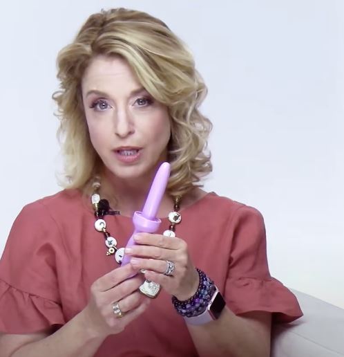 Female pelvic health expert holding a pink vaginal dilator, demonstrating pelvic floor therapy use for vaginismus, vaginal stenosis, and pelvic muscle rehabilitation in a clinical education setting.