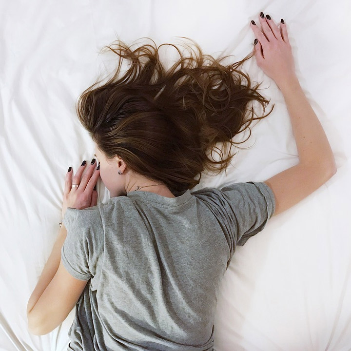 Lack Of Sleep Could Be The Reason You Aren't Losing Weight...-StressNoMore. Woman lying face-down on a bed with arms outstretched, illustrating exhaustion, fatigue, poor sleep or the need for deep rest, suitable for sleep health and wellbeing.