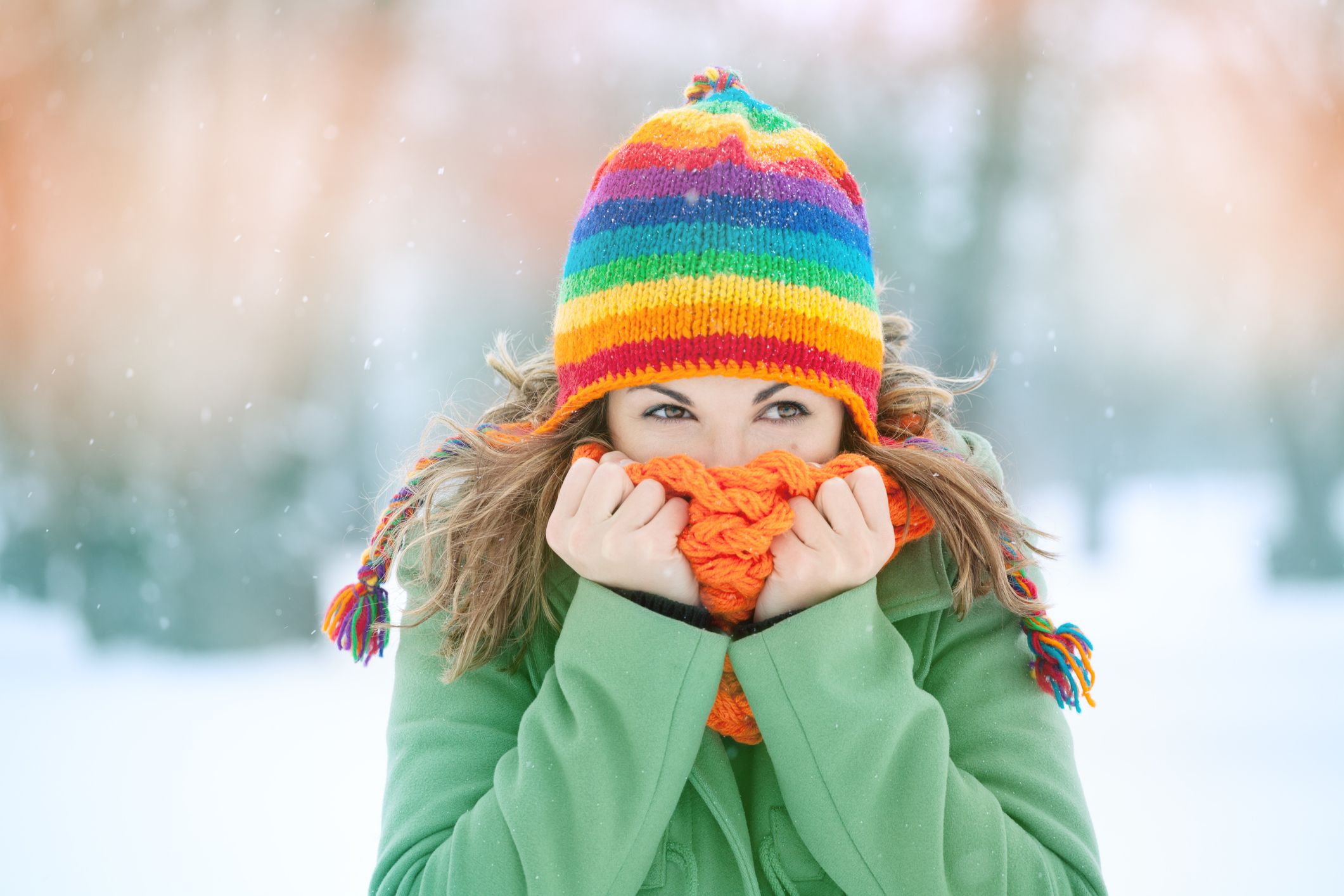 Cheerful winter scene with a person in a rainbow hat and bright scarf standing in the snow, visually supporting the theme ‘Defeat the Winter Blues’ by showing warmth and colour in cold weather. Defeat the Winter Blues!-StressNoMore. 