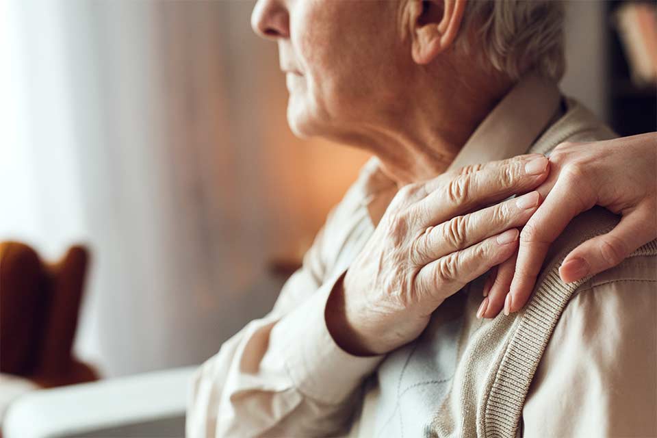 Watch Out for These Early Signs of Dementia-StressNoMore. Older adult sitting with a hand placed supportively on their shoulder, symbolising comfort, care and emotional support