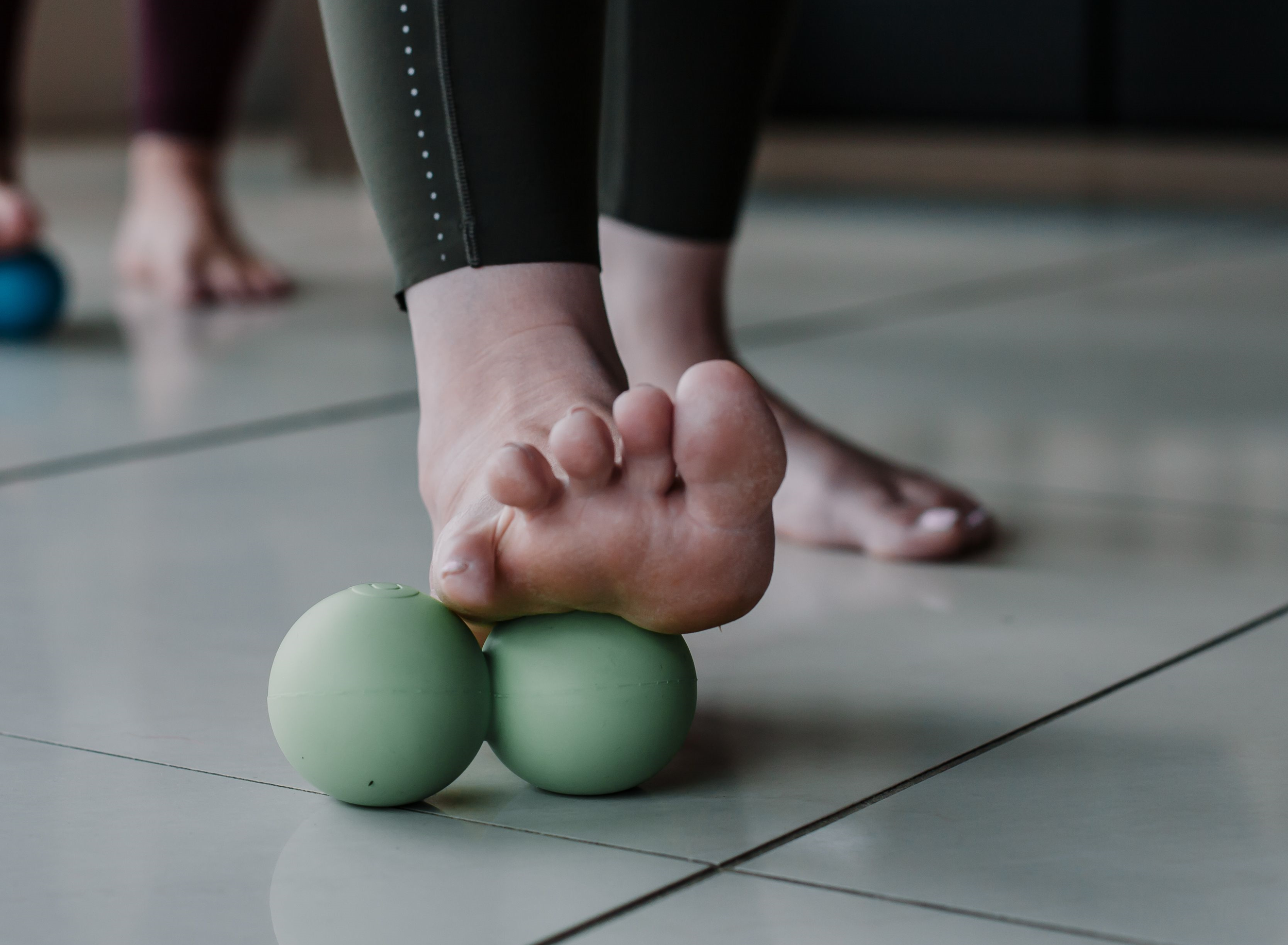 Yoga Tune Up - The Latest Fitness Trend To Sweep the UK-StressNoMore. Foot rolling on a green double massage ball, illustrating plantar fasciitis relief, foot massage, arch support, mobility improvement and tension release.
