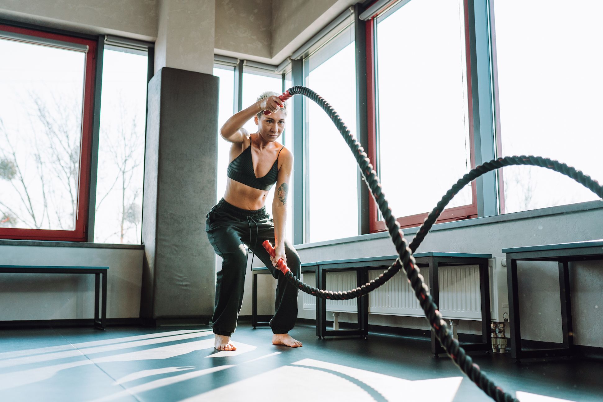 How To Stick With Your January Fitness Goals-StressNoMore. Woman working out with battle ropes in a gym, representing motivation, strength and commitment to achieving January fitness goals.