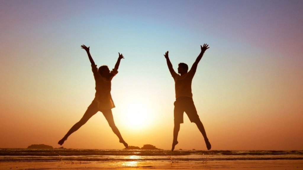 Is The End Of Summer Getting You Down? Get Happy With A SAD Lamp!-StressNoMore. Two people jumping with arms raised on a beach at sunset, symbolising improved mood and energy associated with light therapy for seasonal affective disorder.