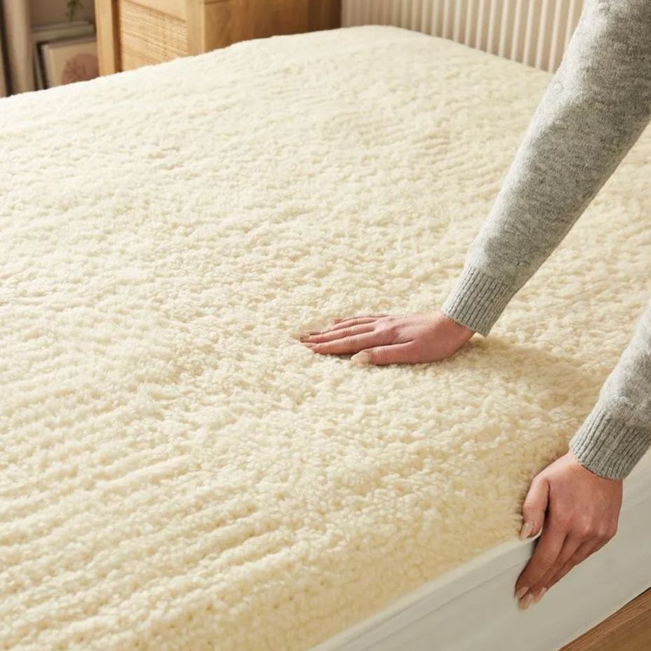 Hands smoothing a soft Beurer heated mattress cover with teddy fleece finish for secure, cosy bed warmth