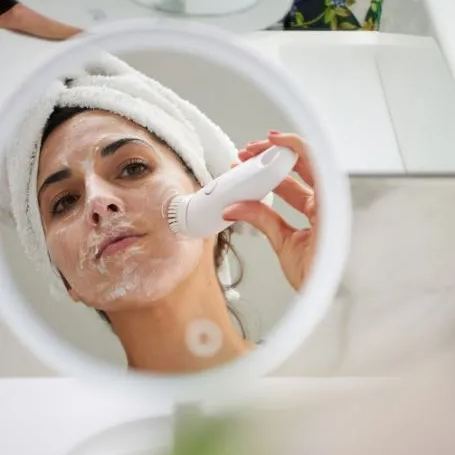 Woman using Beurer FC45 facial cleansing brush during skincare routine, gently exfoliating face for deep pore cleansing and smoother, radiant skin