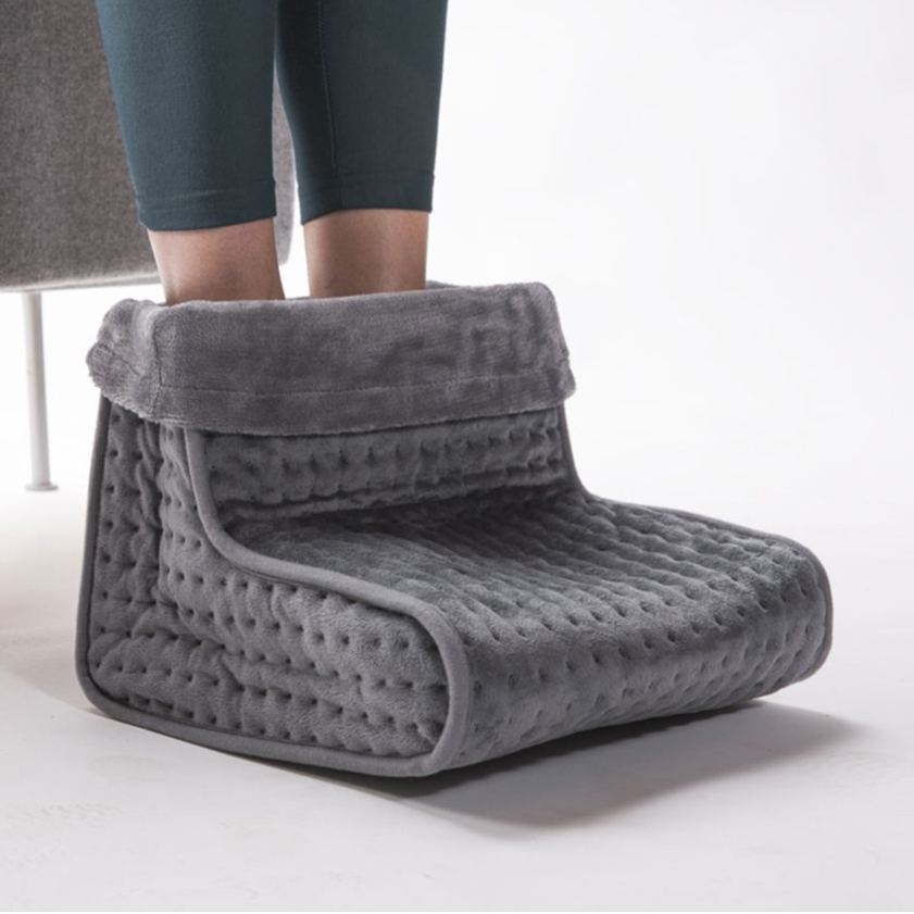Close-up of a grey Lanaform electric heated foot warmer with feet inside, showing the soft padded design used to gently warm feet, improve circulation, and relieve cold or poor circulation while sitting indoors.
