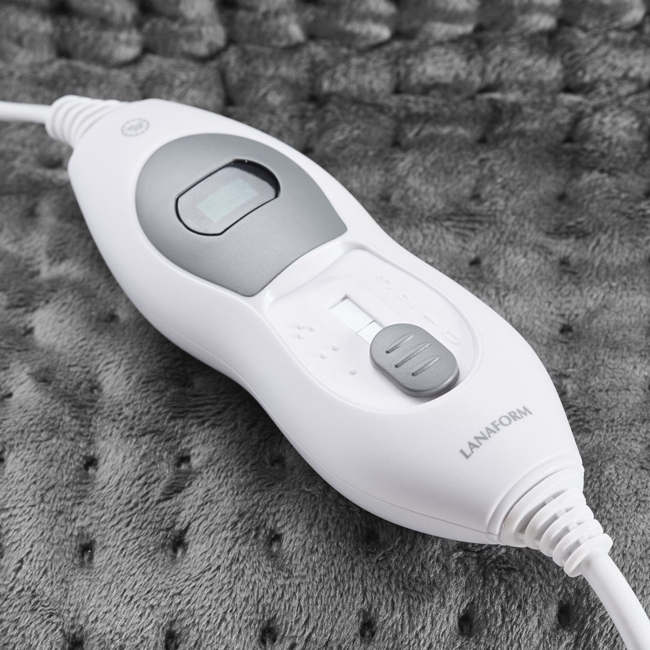 Close-up of Lanaform electric heated foot warmer controller with adjustable heat settings and safety timer, shown on soft grey fabric, allowing easy temperature control for comfortable and safe foot warming.