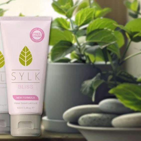 SYLK BLISS natural water-based lubricant tube displayed beside green plants and smooth stones, highlighting plant-based, gentle intimate lubricant with new formula designed to support comfort, hydration, and a natural, calming experience.