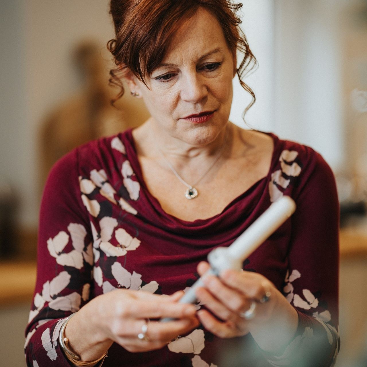 Adult woman holding and examining a white medical dilator applicator indoors, demonstrating correct handling for pelvic floor therapy or clinical use in a calm, professional setting.