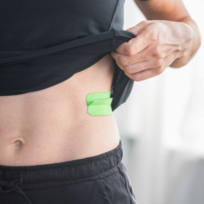 Green kinesiology tape with activation flap applied to the lower abdomen, demonstrating deep tissue and fascia stimulation for improved circulation, lymphatic drainage, muscle support and physiotherapy treatment.
