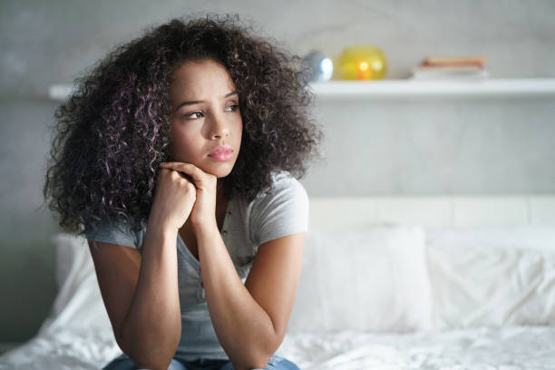 Woman sitting on a bed with a worried expression, used to illustrate symptoms like painful periods and raise awareness about endometriosis and its impact. Painful Periods? Get the Facts on Endometriosis-StressNoMore