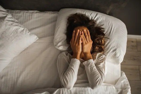 Person in bed covering their face, illustrating tiredness, stress, poor sleep or night time discomfort, suitable for content on insomnia, menopause symptoms, fatigue or mental wellbeing. How Does Sleep Affect Weight Loss?-StressNoMore