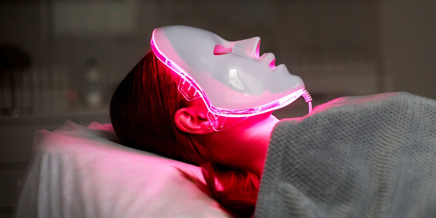 Person lying on a treatment bed wearing an LED light therapy facial mask glowing red, receiving a skincare or beauty treatment in a spa setting. Shining the Light on Low Level Light Therapy-StressNoMore