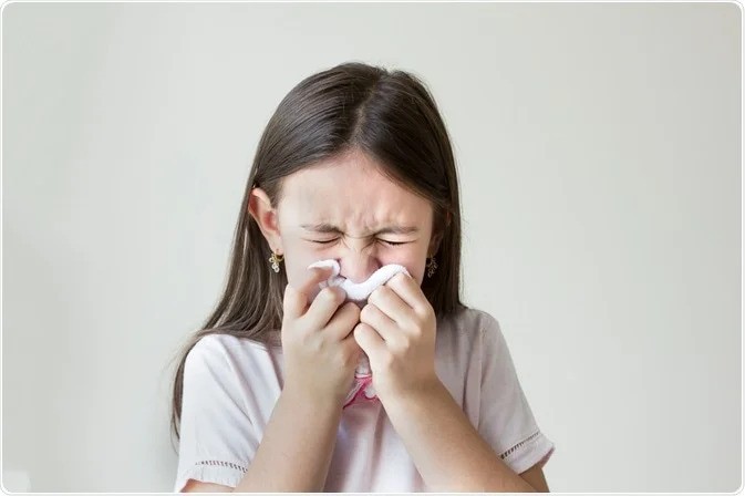 Child sneezing into a tissue against a plain background, illustrating symptoms that may be caused by allergens such as dust mites. Do You Have Dust Mites?-StressNoMore