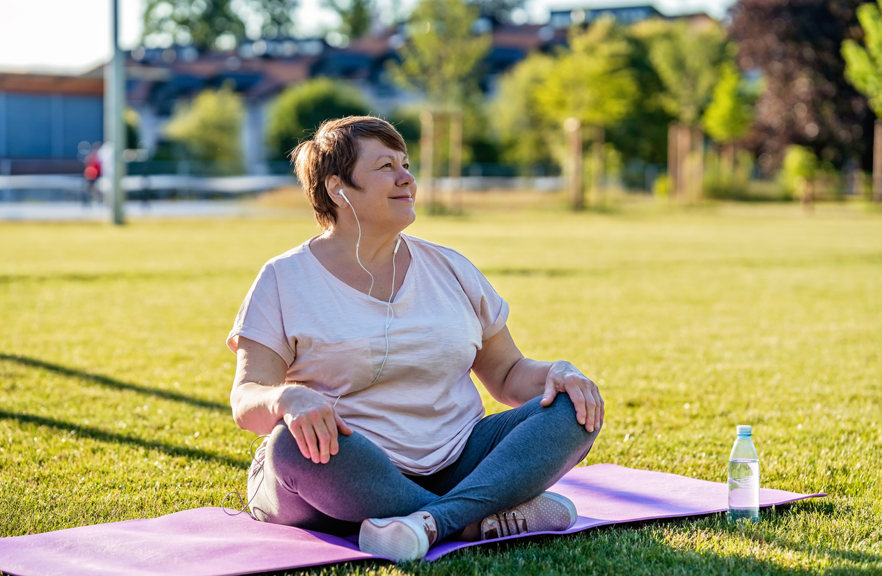 Older woman sat on yoga mat in the park, getting ready to exercise.