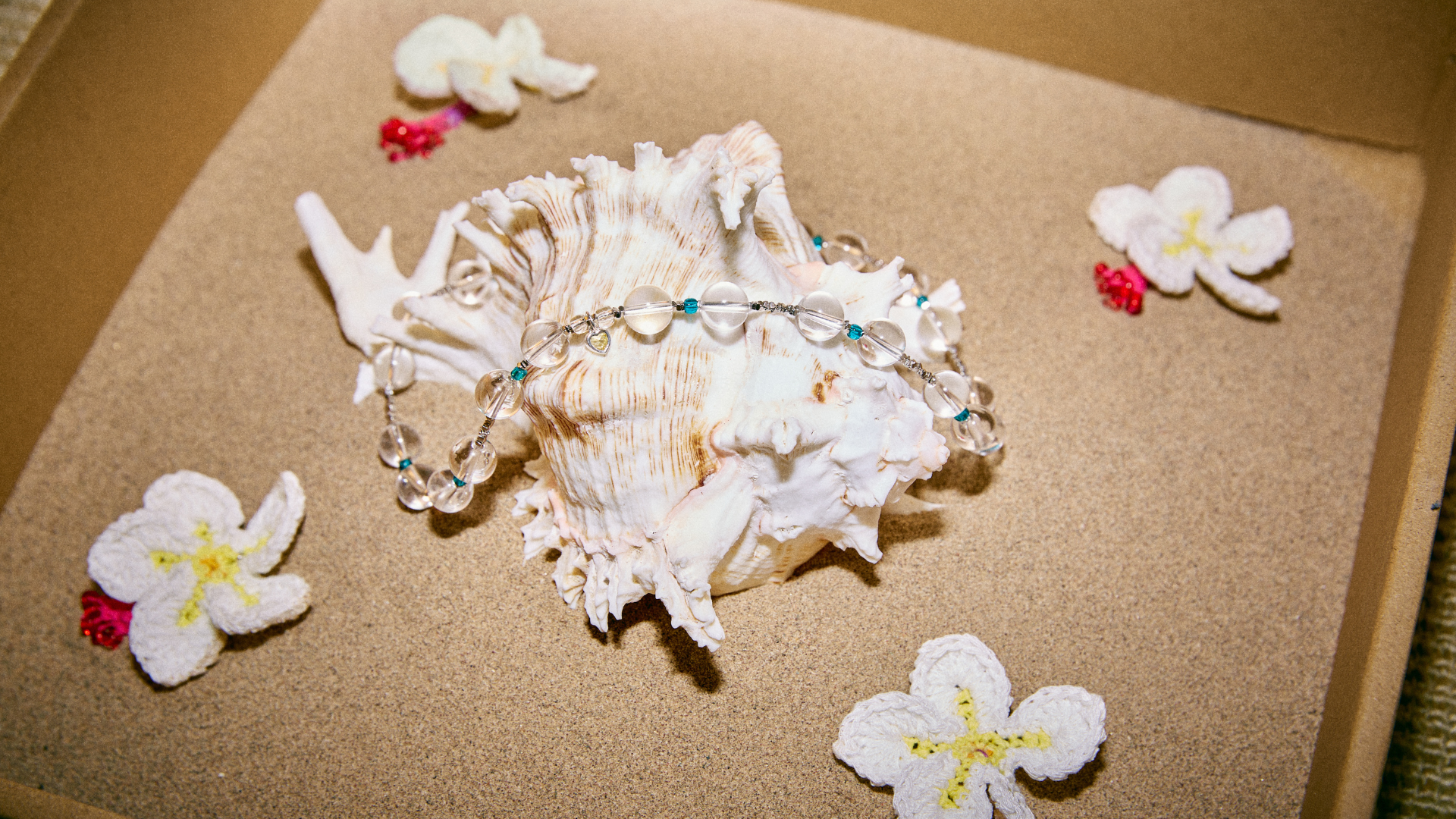 Elegant artisan-made bracelet featuring crystal beads, staged with seashells and plumeria flowers, a dreamy accessory for a beach vacation look from FeekyStore.