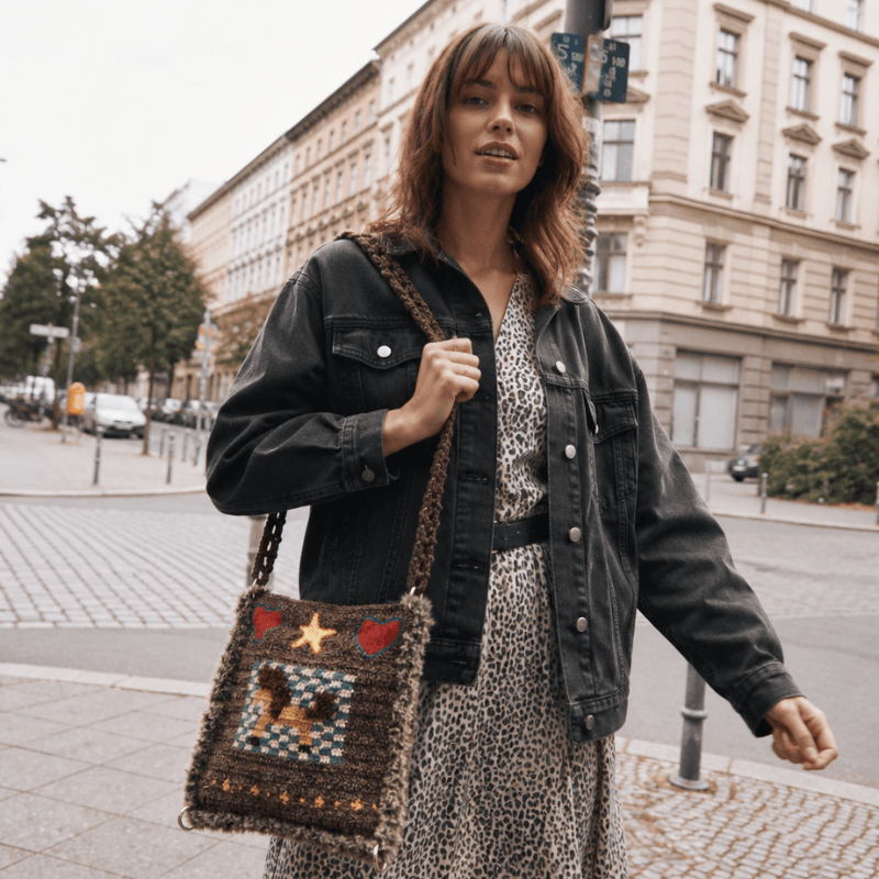 FeekyStore handmade crochet unicorn pony bag with colorful details, modeled as a crossbody bag by a woman in a city street with a denim jacket.