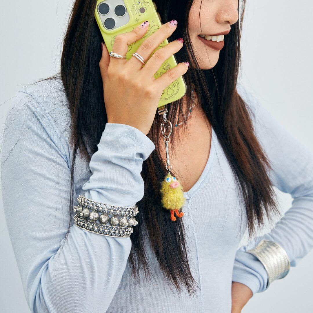 A creative accessory shot showing the Feeky duckling charm attached to a bright yellow phone case, highlighting its playful design.