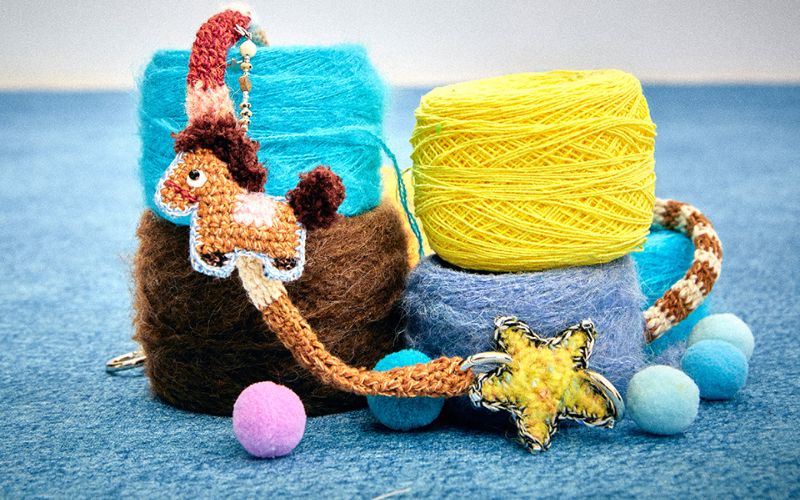 {"default":"Hand-hooked crochet pony charm next to vibrant blue and yellow yarn balls, highlighting the artisanal fiber art process."}
