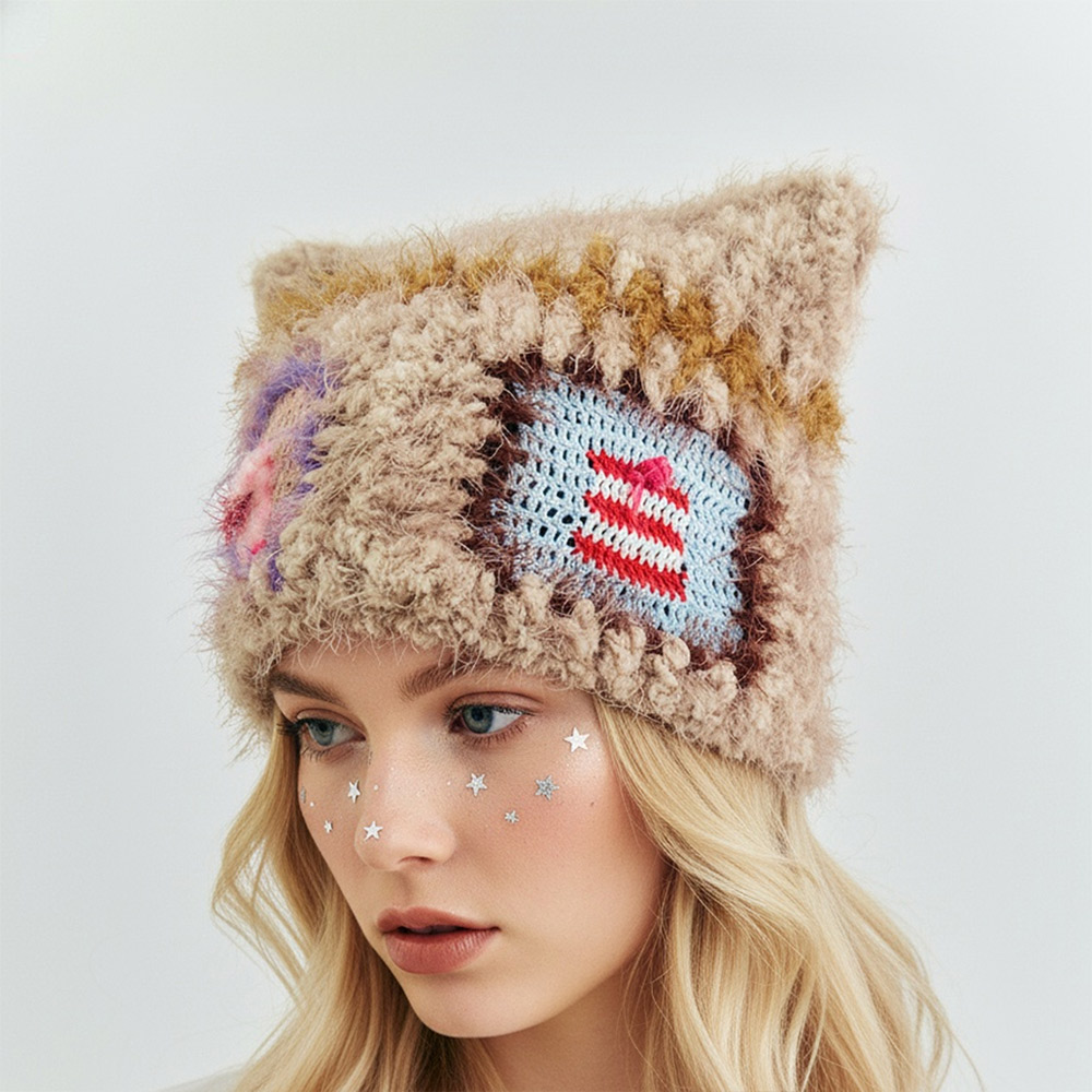 An angled front view of a model wearing the Cat Star Crochet Hat, featuring textured beige yarn, cat ears, and a blue and red striped granny square detail.