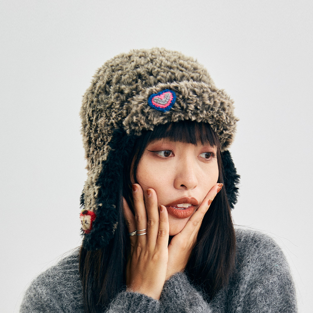An angled three-quarter view of the Cloud-Pooch Crochet trapper hat, displaying the vibrant yellow graphic patch and dangling earflap accessories.