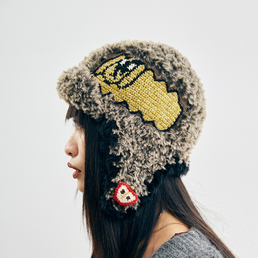 Front view of a model wearing the fuzzy Cloud-Pooch Crochet Aviator Hat, showcasing the thick plush textured brim and a colorful heart detail on the front.