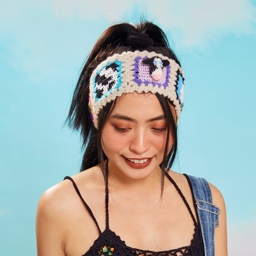 Full front view of a model wearing the Cow Velvet Crochet Headband, highlighting the prominent black and white cow print granny square patch.