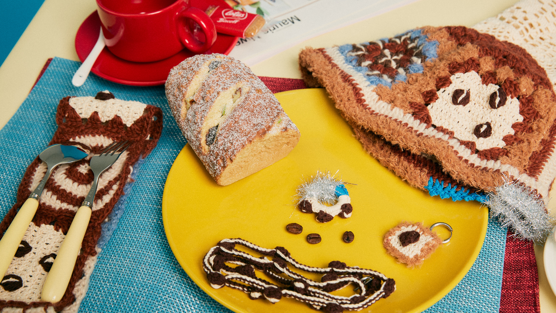 A collection of vibrant dopamine-style crochet handicrafts displayed with a yellow plate, bread, and a red coffee cup