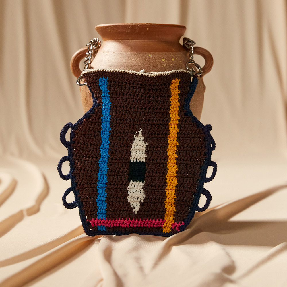 The eye color matching vase crochet bag fitted seamlessly over an earthen pottery vase, presenting an artisan lifestyle aesthetic and detailed geometric motifs.