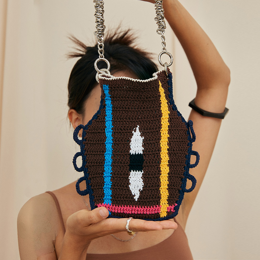 Front view of a model holding the Eye Color Matching Vase Crochet Bag, highlighting the vase-like silhouette, center eye motif, and metallic silver shoulder chain.