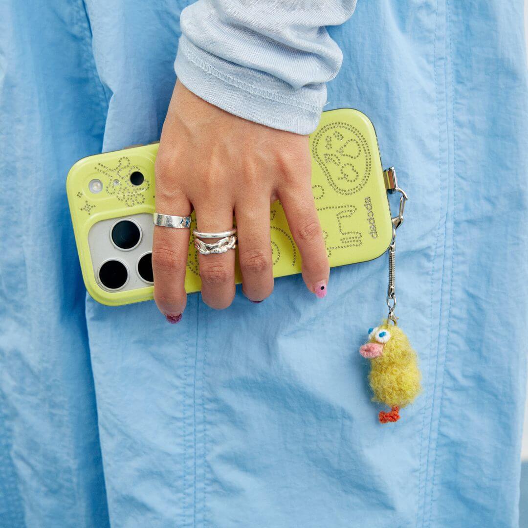 A creative accessory shot showing the Feeky duckling charm attached to a bright yellow phone case, highlighting its playful design.