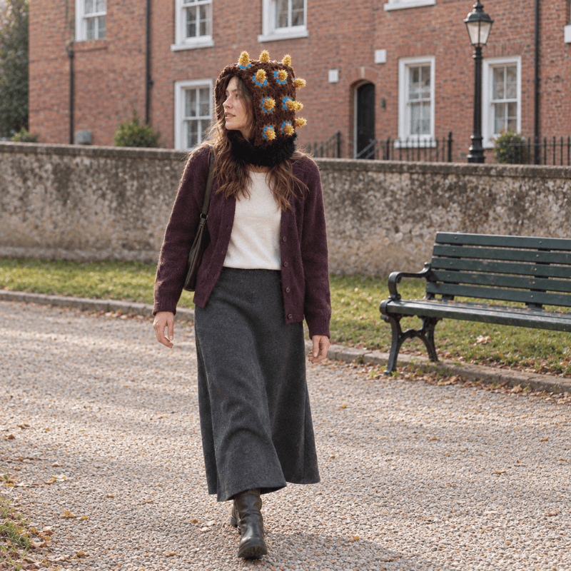 FeekyStore brown bomb hat with distinct gold spikes, modeled by a woman walking in an English style park wearing a dark cardigan and skirt.