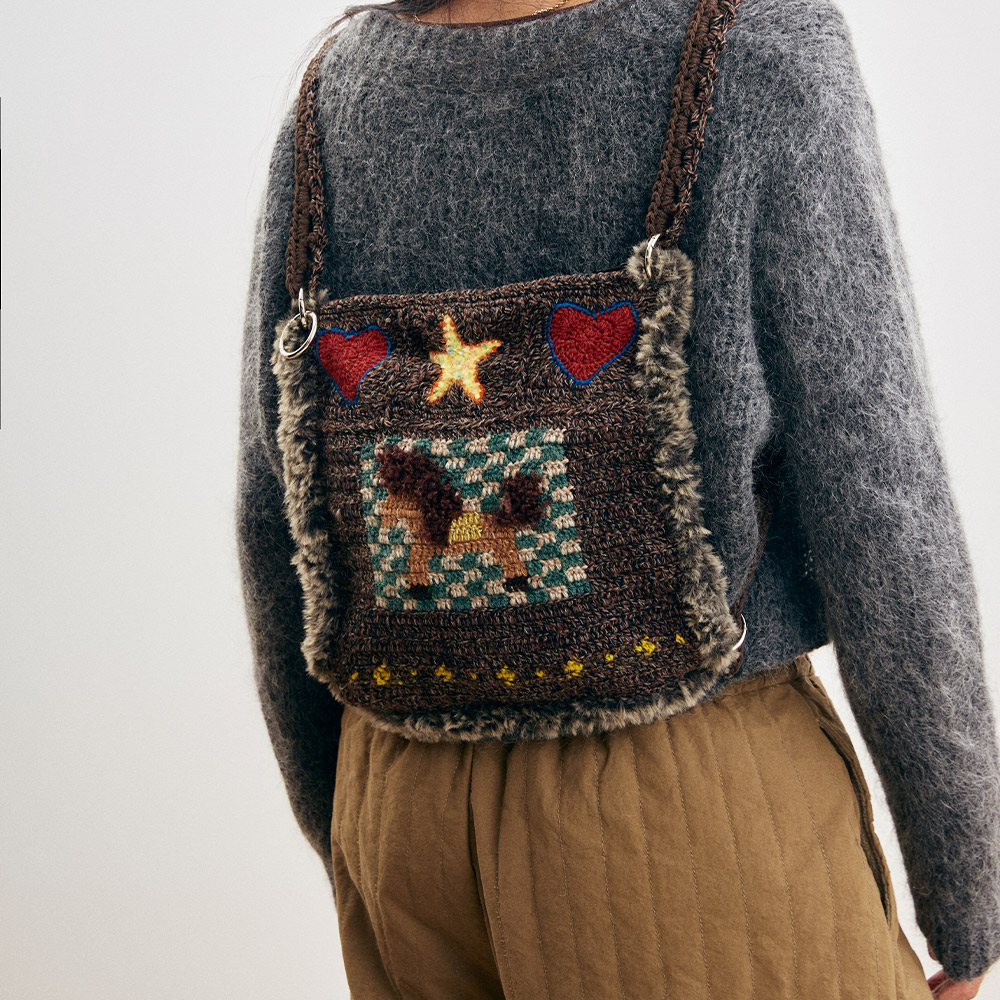 Back view of a model styling the transformable little pony crochet bag as a cozy dual-strap winter backpack over a grey sweater.