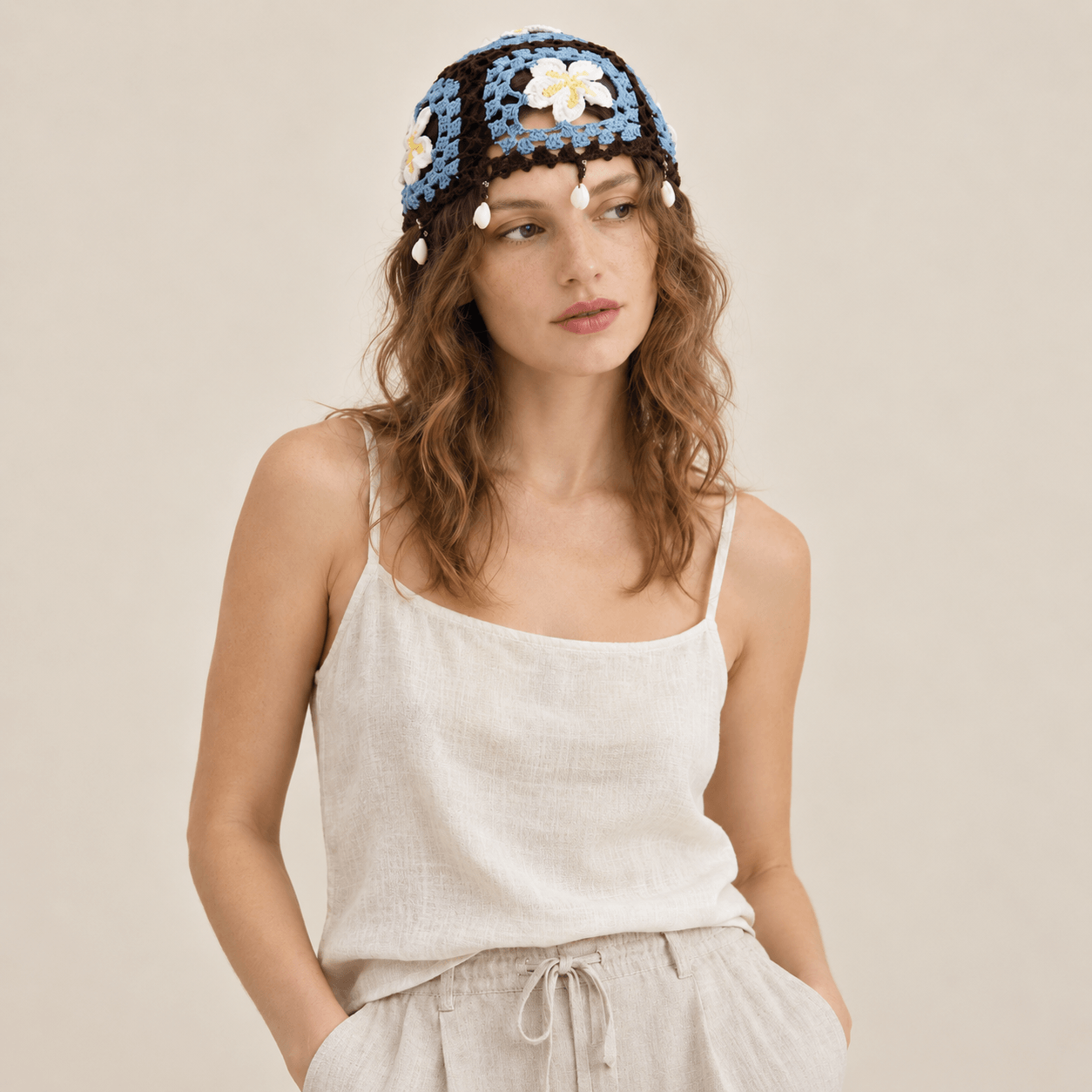 FeekyStore brown and blue crochet cap featuring plumeria flower motifs and dangling shell tassels, worn by a model in a clean studio setting.