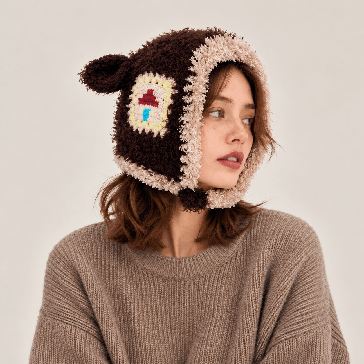 Model wearing the Little Lamb Patchwork Hat with a brown sweater, showing its playful shape and colorful crochet patches.