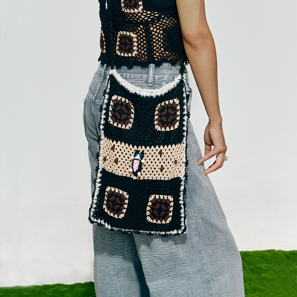 Side profile of a model wearing the Lying Flat Cat Crochet Bag, displaying the granny square geometric patches and the central miniature cat motif.