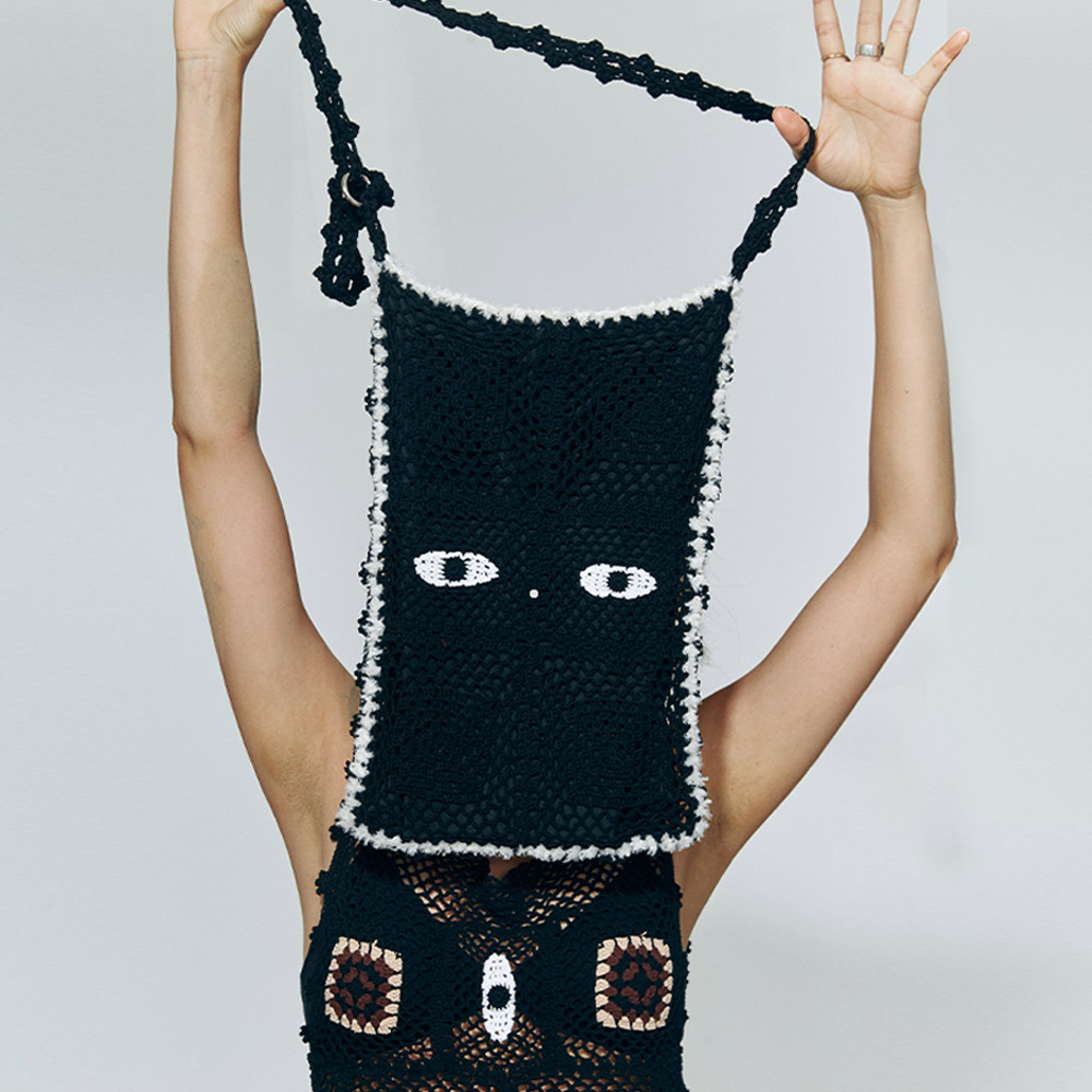 Front view of the reversible crochet crossbody bag held up by a model, showcasing the black side with a striking white cat eyes stitch pattern.