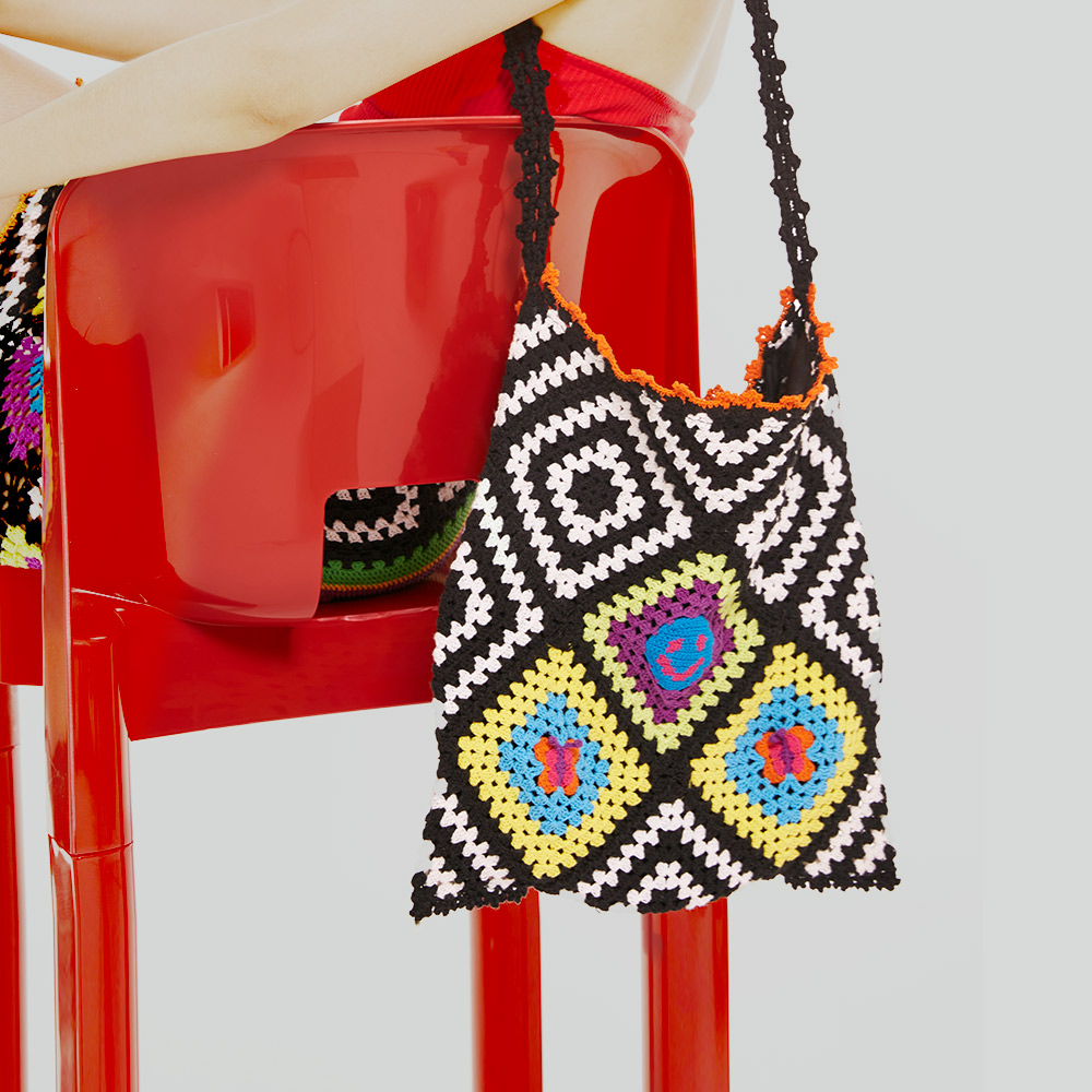 Product display of the Patchwork Crochet Shoulder Bag hanging on a sleek red chair, highlighting the black and white diamond pattern and beaded top border.
