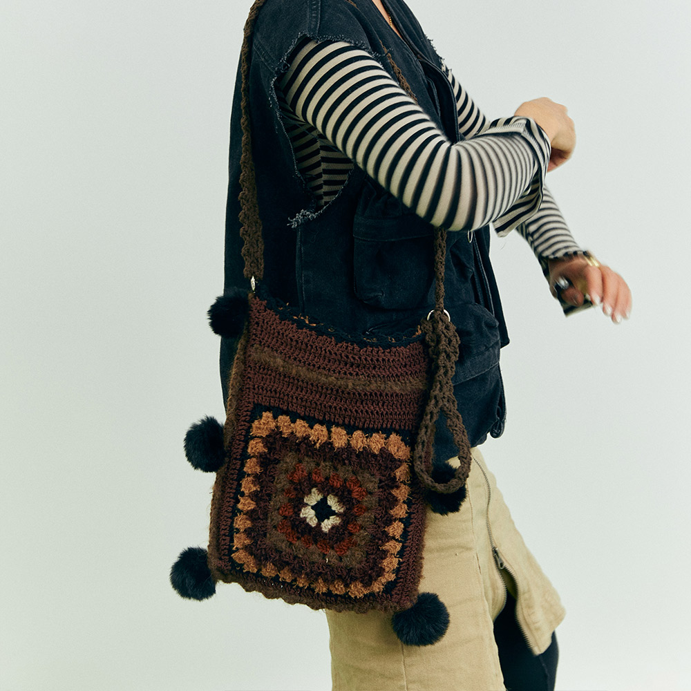 A model holding the long strap of the puppy theme crochet shoulder bag downwards, paired with retro brown cowboy boots for an autumn western look.